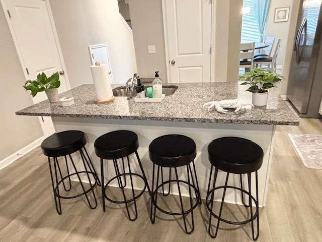 kitchen featuring sink, light wood-type flooring, a breakfast bar area, stainless steel fridge, and light stone counters