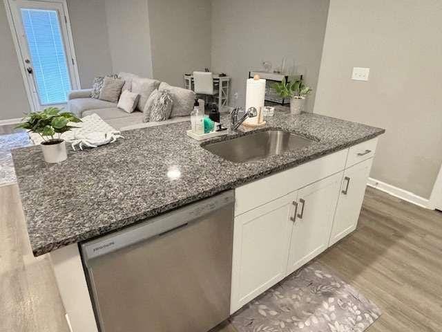 kitchen with white cabinets, dishwasher, dark stone countertops, sink, and a center island with sink