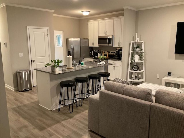 kitchen with an island with sink, a kitchen breakfast bar, stainless steel appliances, and white cabinetry