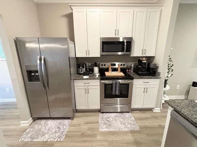 kitchen with light hardwood / wood-style flooring, stainless steel appliances, ornamental molding, white cabinets, and dark stone counters