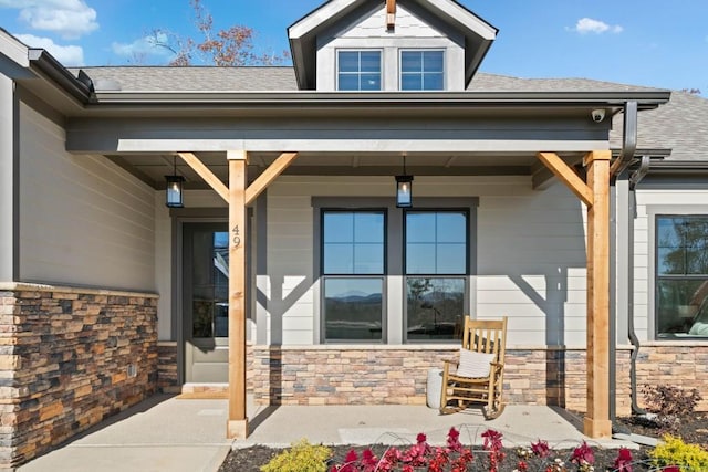 property entrance with stone siding, a porch, and a shingled roof