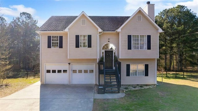 bi-level home featuring a front lawn, fence, concrete driveway, a chimney, and a garage