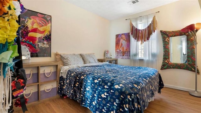 bedroom with wood finished floors, visible vents, and baseboards