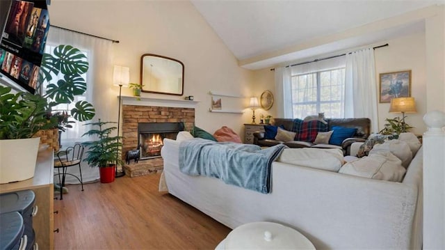 living area with a stone fireplace, lofted ceiling, and wood finished floors