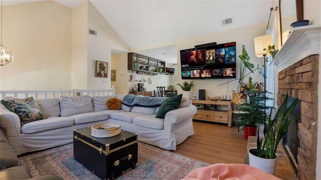 living area with wood finished floors, visible vents, high vaulted ceiling, a fireplace, and a chandelier