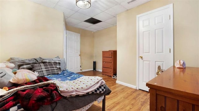 bedroom featuring visible vents, light wood-style flooring, a paneled ceiling, and baseboards