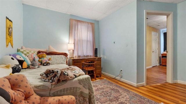 bedroom featuring a drop ceiling, baseboards, and wood finished floors