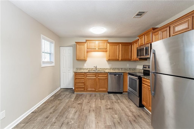 kitchen with light stone countertops, light wood-type flooring, a textured ceiling, stainless steel appliances, and sink