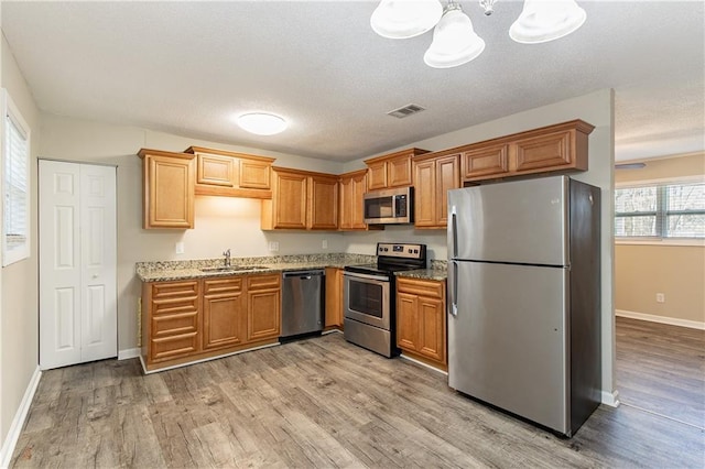 kitchen featuring light stone countertops, appliances with stainless steel finishes, sink, decorative light fixtures, and light hardwood / wood-style floors