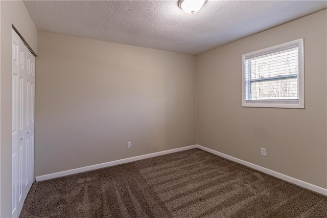 spare room featuring dark carpet and a textured ceiling