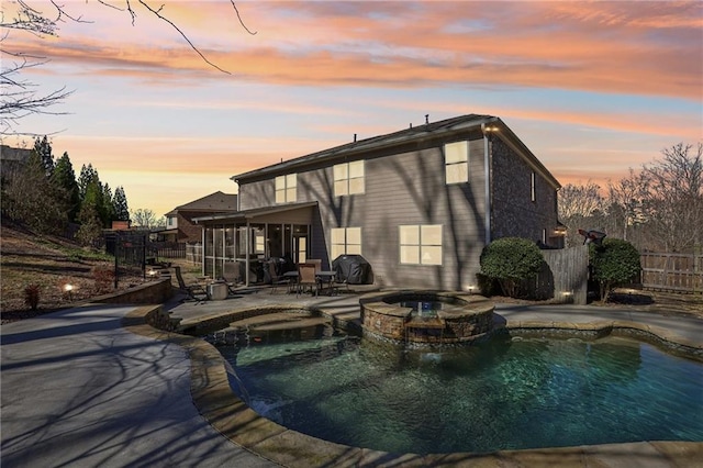 back of property at dusk featuring a patio, fence, a pool with connected hot tub, and a sunroom