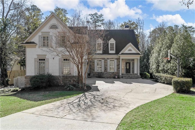 view of front of property featuring stone siding, a front lawn, fence, and driveway