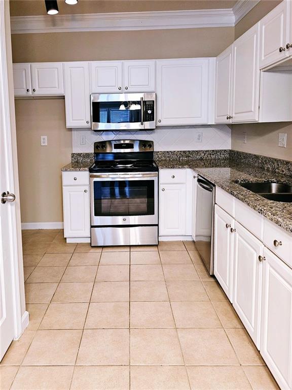 kitchen featuring stainless steel appliances, light tile patterned floors, crown molding, white cabinetry, and dark stone counters