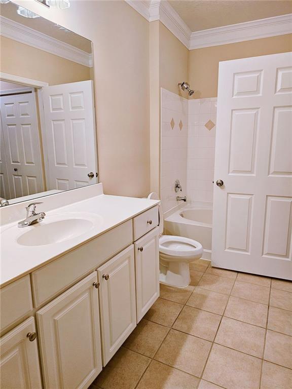 full bathroom featuring tile patterned flooring, tiled shower / bath combo, toilet, vanity, and ornamental molding