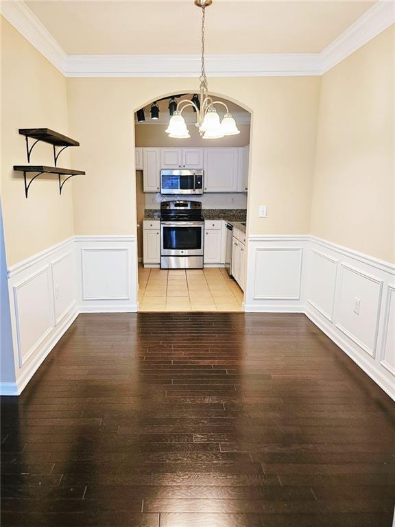 kitchen with stainless steel appliances, white cabinets, ornamental molding, and pendant lighting