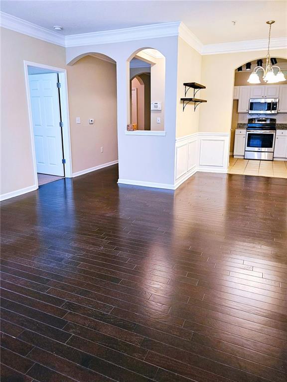 unfurnished living room featuring a notable chandelier, crown molding, and dark hardwood / wood-style floors