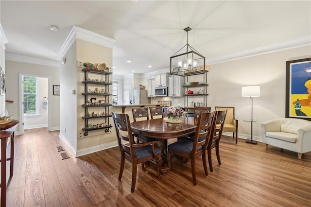 dining area with hardwood / wood-style floors, crown molding, and an inviting chandelier