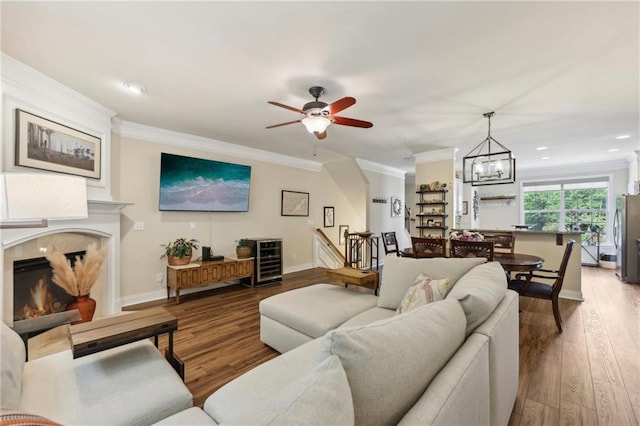 living room with wood-type flooring, ceiling fan with notable chandelier, and crown molding