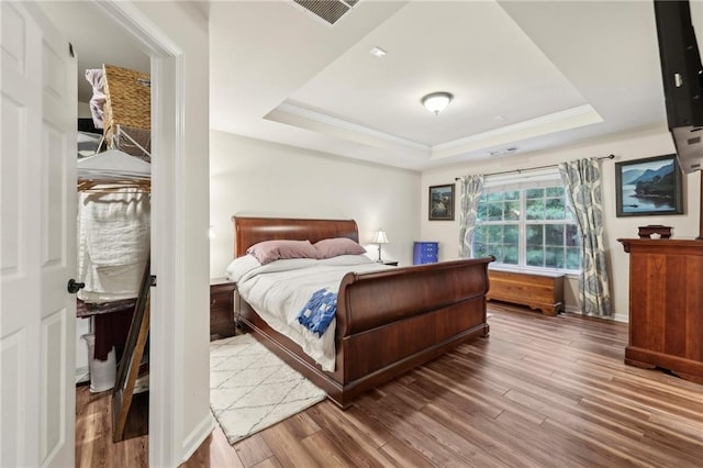 bedroom featuring wood-type flooring, a raised ceiling, and ornamental molding