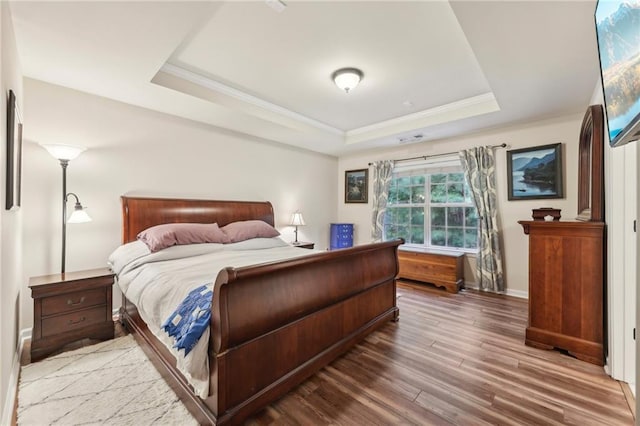 bedroom featuring wood-type flooring, crown molding, and a raised ceiling