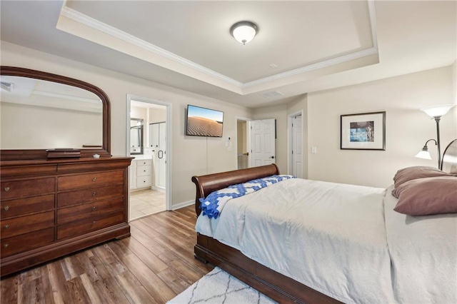 bedroom with ensuite bathroom, wood-type flooring, ornamental molding, and a tray ceiling