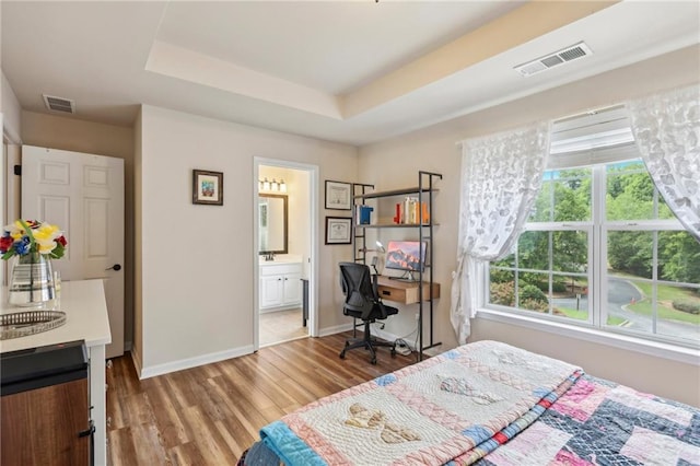 bedroom with ensuite bathroom, light hardwood / wood-style floors, and a tray ceiling