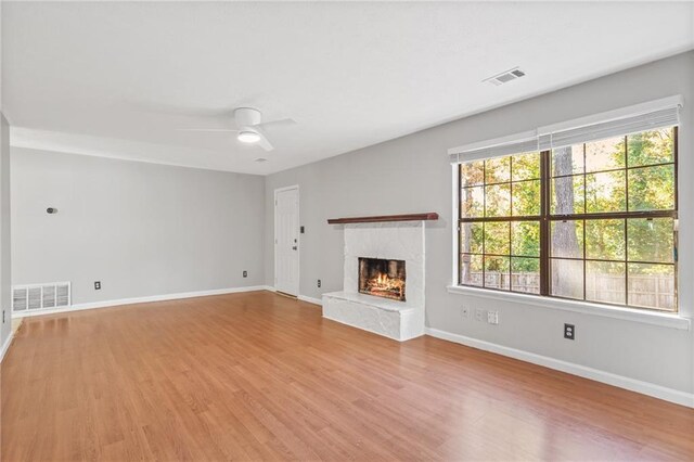 unfurnished living room with a premium fireplace, ceiling fan, and light wood-type flooring