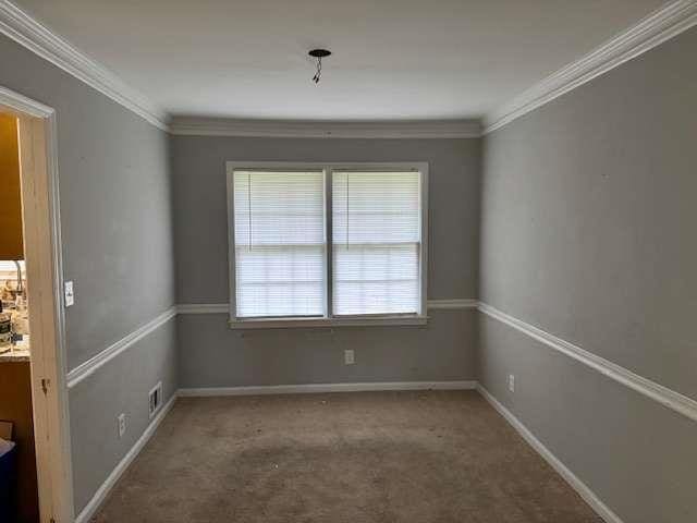 carpeted empty room with baseboards, visible vents, and ornamental molding