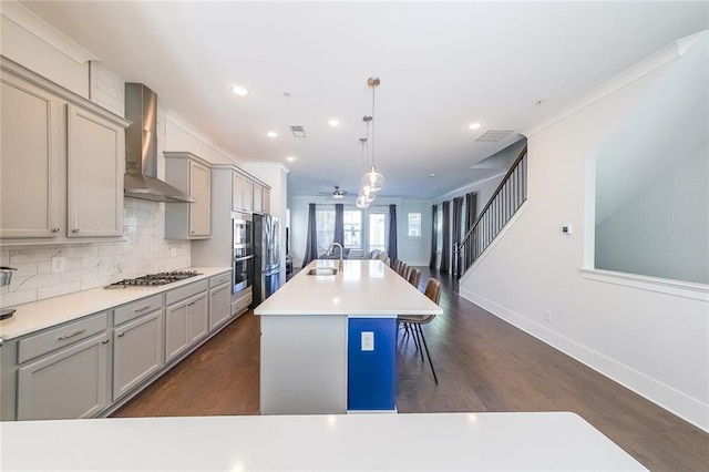 kitchen featuring backsplash, gray cabinetry, appliances with stainless steel finishes, a sink, and wall chimney exhaust hood