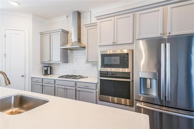 kitchen featuring stainless steel appliances, gray cabinets, a sink, and wall chimney range hood