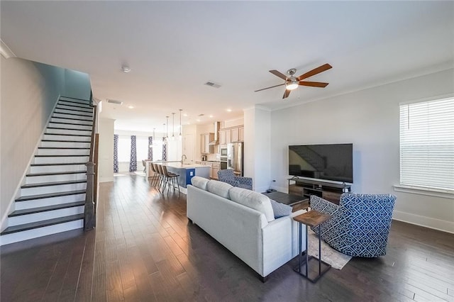 living area featuring ceiling fan, visible vents, baseboards, stairs, and dark wood finished floors