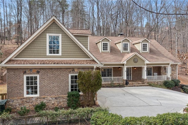 view of front of property with stone siding, a porch, a shingled roof, and brick siding