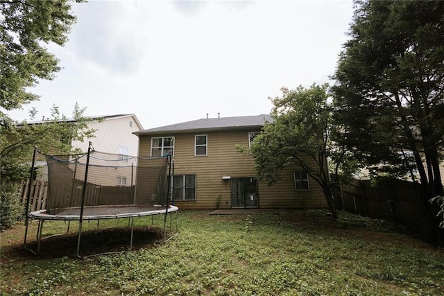 rear view of property with a trampoline and a lawn