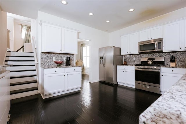 kitchen featuring white cabinets, decorative backsplash, light stone countertops, appliances with stainless steel finishes, and dark hardwood / wood-style flooring