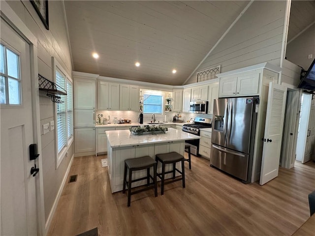 kitchen with vaulted ceiling, appliances with stainless steel finishes, a kitchen breakfast bar, a kitchen island, and white cabinets