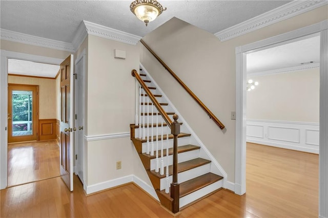 staircase with wood finished floors, wainscoting, crown molding, a decorative wall, and a textured ceiling