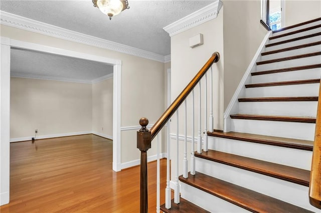 stairs with wood finished floors, a textured ceiling, baseboards, and ornamental molding