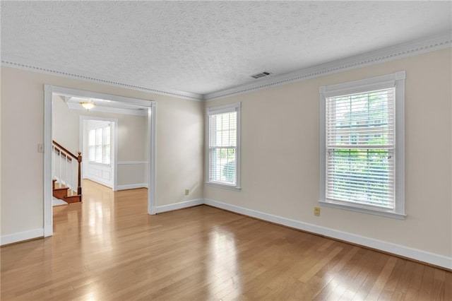 empty room with ornamental molding, light wood finished floors, healthy amount of natural light, stairway, and a textured ceiling