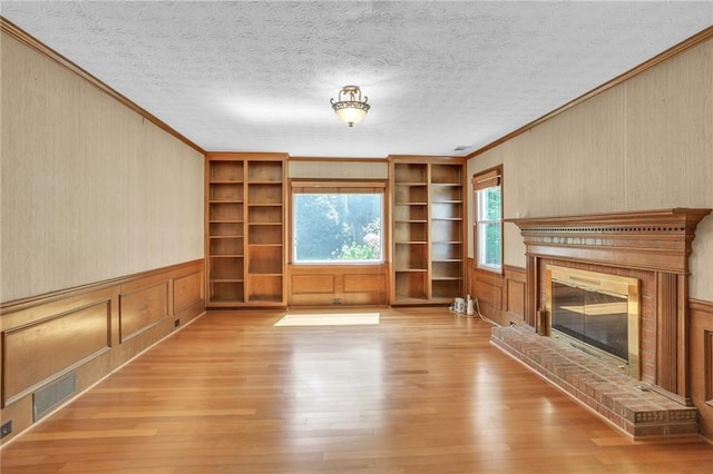 unfurnished living room featuring crown molding, built in features, wood-type flooring, a fireplace, and a textured ceiling