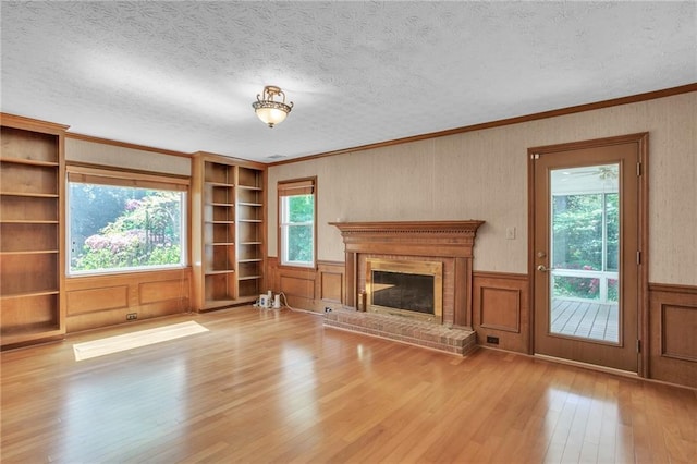 unfurnished living room with hardwood / wood-style flooring, a brick fireplace, a textured ceiling, crown molding, and a wainscoted wall