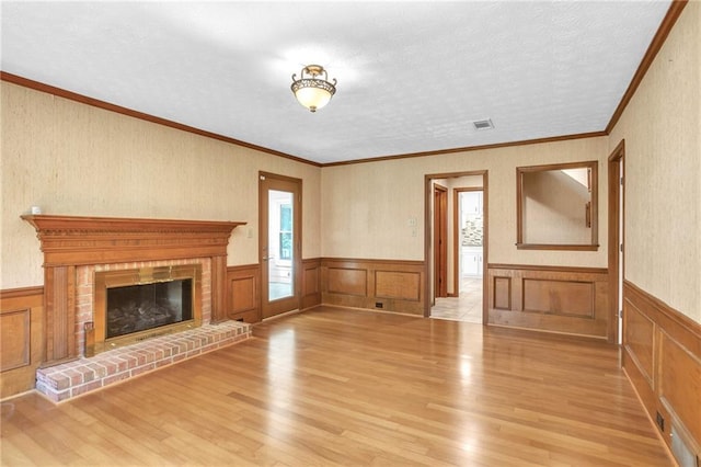 unfurnished living room with wood finished floors, a wainscoted wall, a fireplace, and ornamental molding