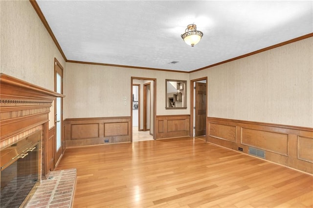 unfurnished living room with a brick fireplace, light wood-type flooring, a wainscoted wall, and ornamental molding