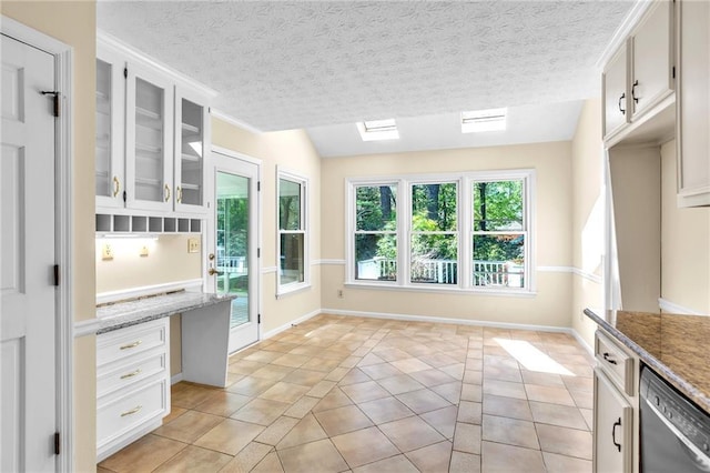 kitchen with stainless steel dishwasher, plenty of natural light, glass insert cabinets, and light tile patterned flooring
