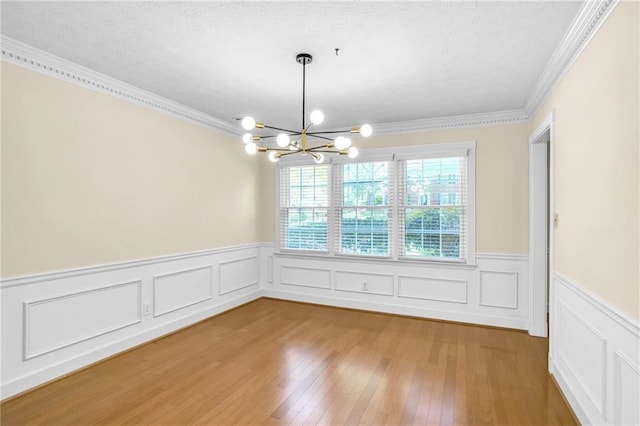 unfurnished dining area featuring a chandelier, ornamental molding, a wainscoted wall, wood finished floors, and a textured ceiling