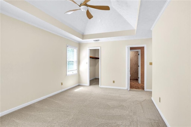 unfurnished bedroom featuring carpet floors, a tray ceiling, baseboards, ceiling fan, and a walk in closet