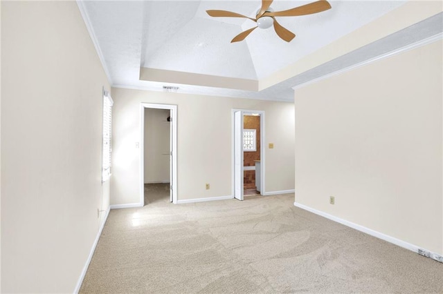 unfurnished bedroom with light carpet, a walk in closet, a raised ceiling, baseboards, and ornamental molding