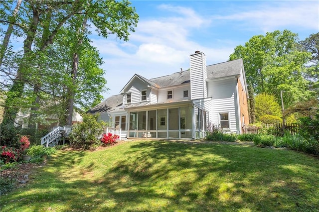rear view of house with a sunroom, a yard, a chimney, and a shingled roof