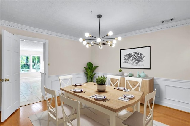 dining space featuring ornamental molding, a chandelier, a wainscoted wall, light wood-style flooring, and a textured ceiling