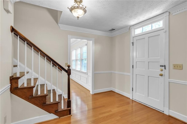 foyer with wood finished floors, a textured ceiling, stairs, and ornamental molding