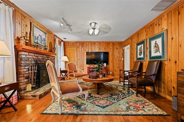 living area with hardwood / wood-style flooring, ceiling fan, a brick fireplace, and wooden walls